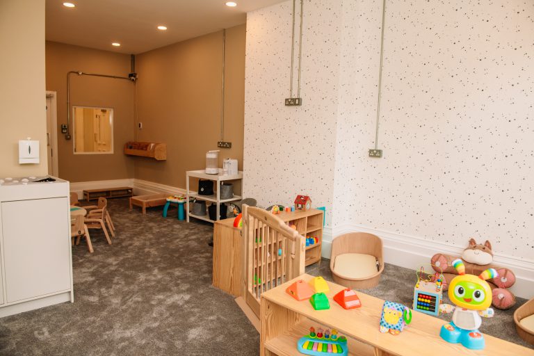A playroom at Leafield House Nursery featuring a wooden shelf filled with colorful toys for children to play with.