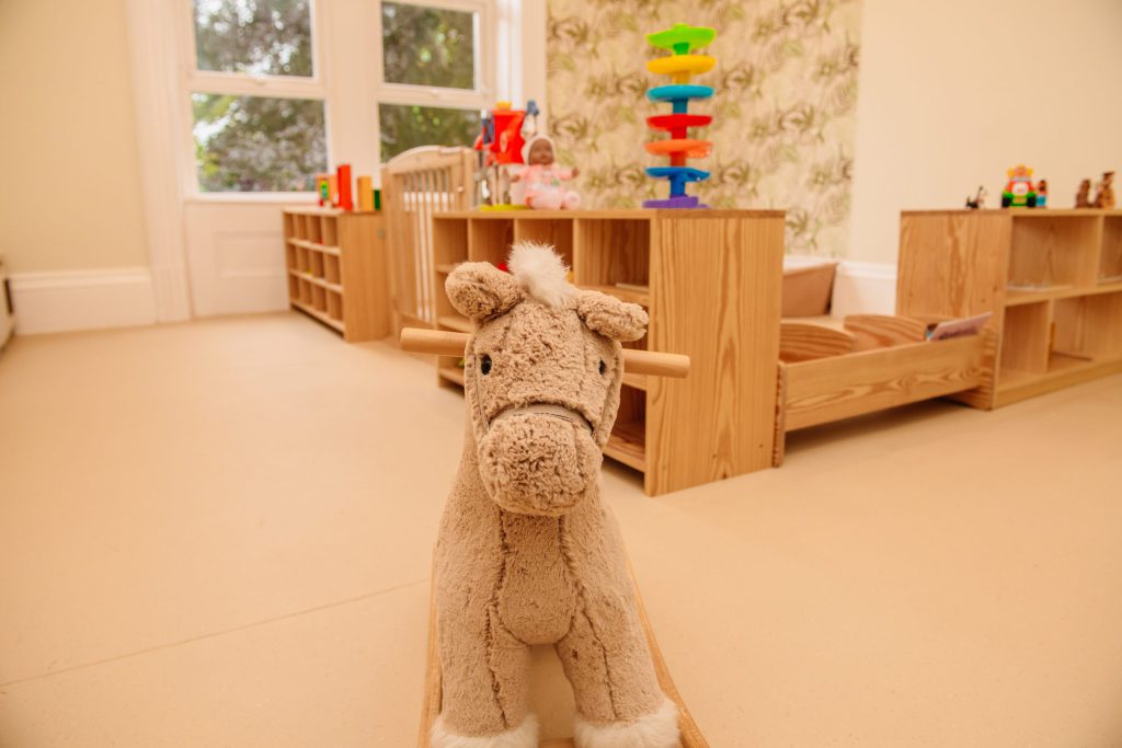 A playroom at Leafield House Nursery featuring a wooden shelf filled with colorful toys for children to play with.