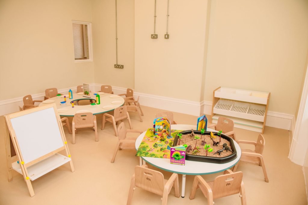 A classroom at Leafield House Nursery featuring a table, chairs, and a chalkboard on the wall.